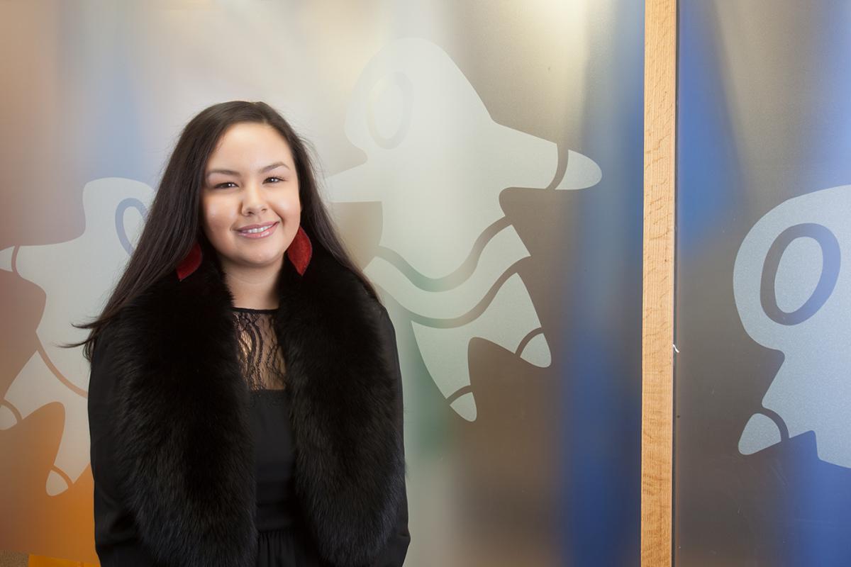 The president of the National Inuit Youth Council Maatalii Okali sitting in front of banner.