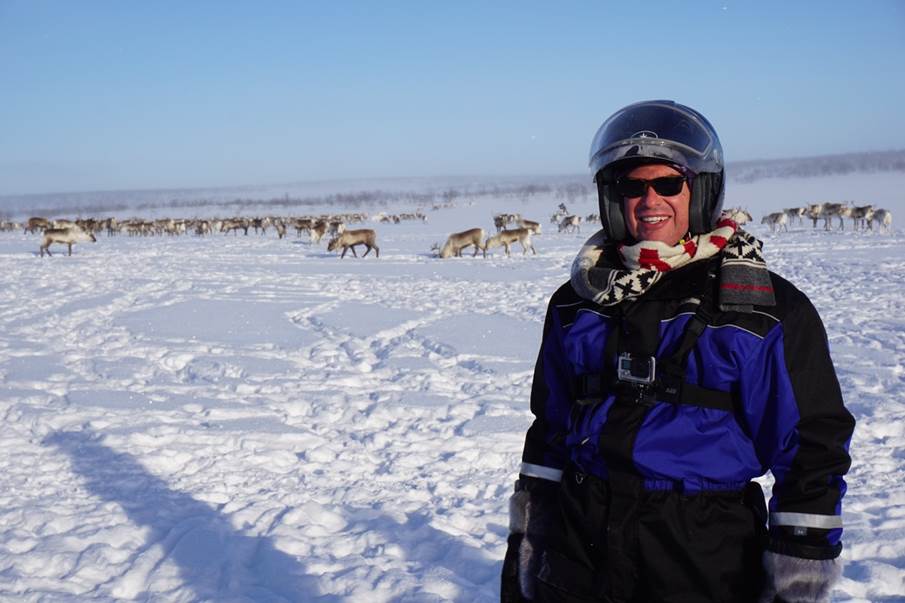 Man standing in front of reindeer herd in snowy landscape