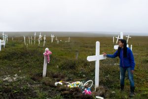 A woman in a cemetery next to a white grave cross