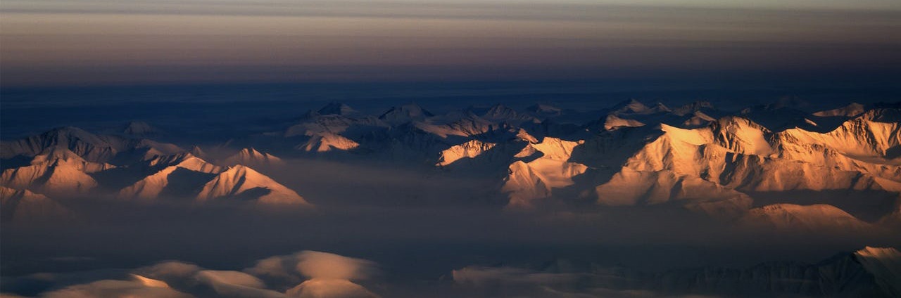 Aerial view of morning sun reflected off mountains in northeastern Greenland with the moon in the sky.