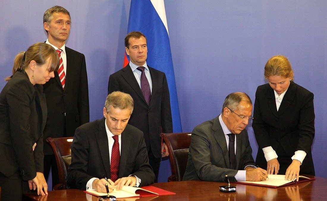 Men sit on table signing a treaty with two women assisting them and two men standing behind them