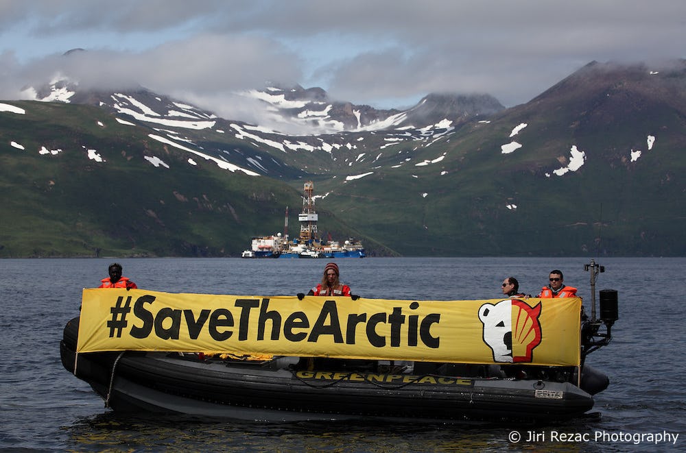 Four people with banner on boat with oil rig in the background