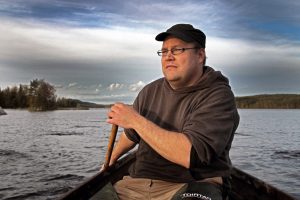 Man sitting in a small paddel boat with lake and forest in the background