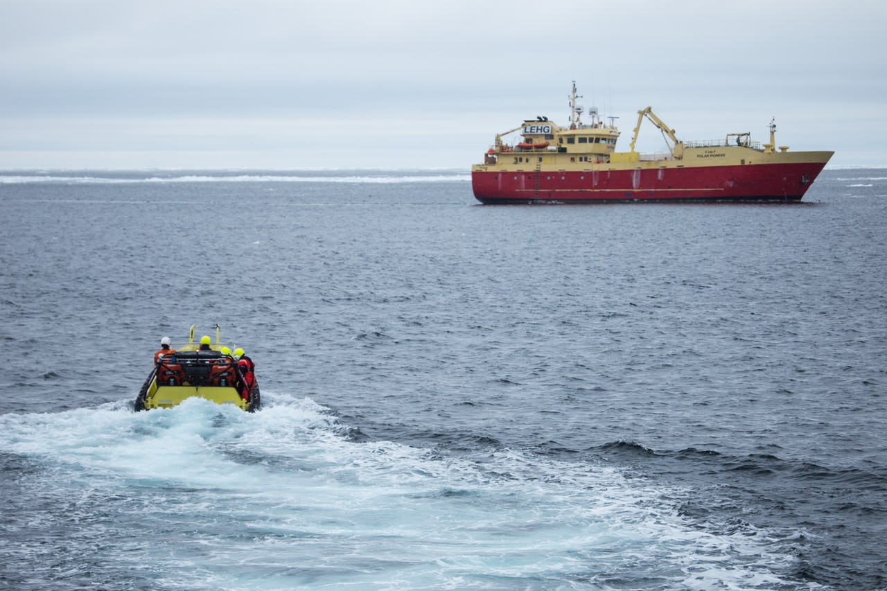 Small boat approaching large boat in Arctic waters.