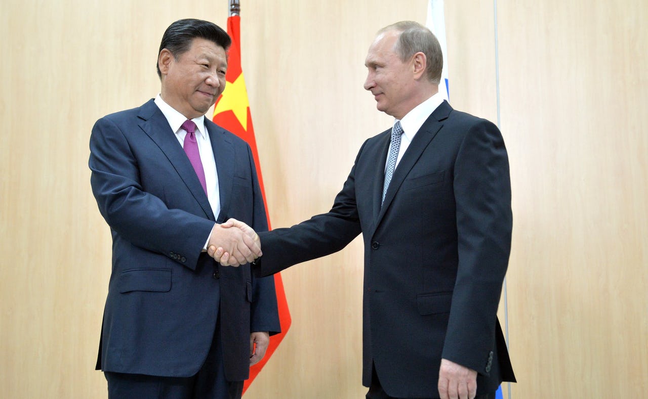 Two men shaking hands in front of two flags