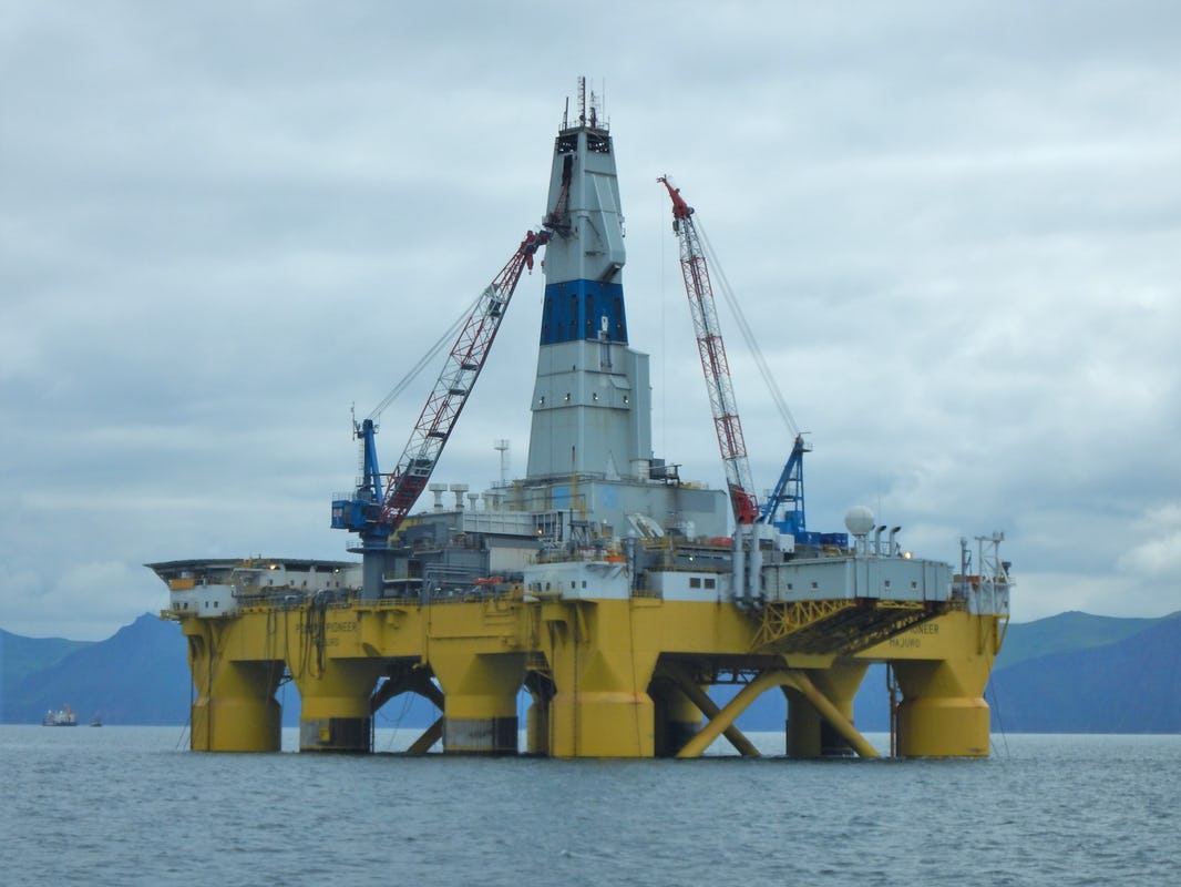 Yellow and white drilling rig standing in waters and grey mountains in the background