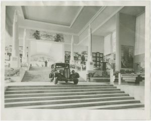 Black and white photo of a car inside an exhibition hall
