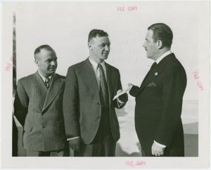 Black and white photo depicting three men in suits talking