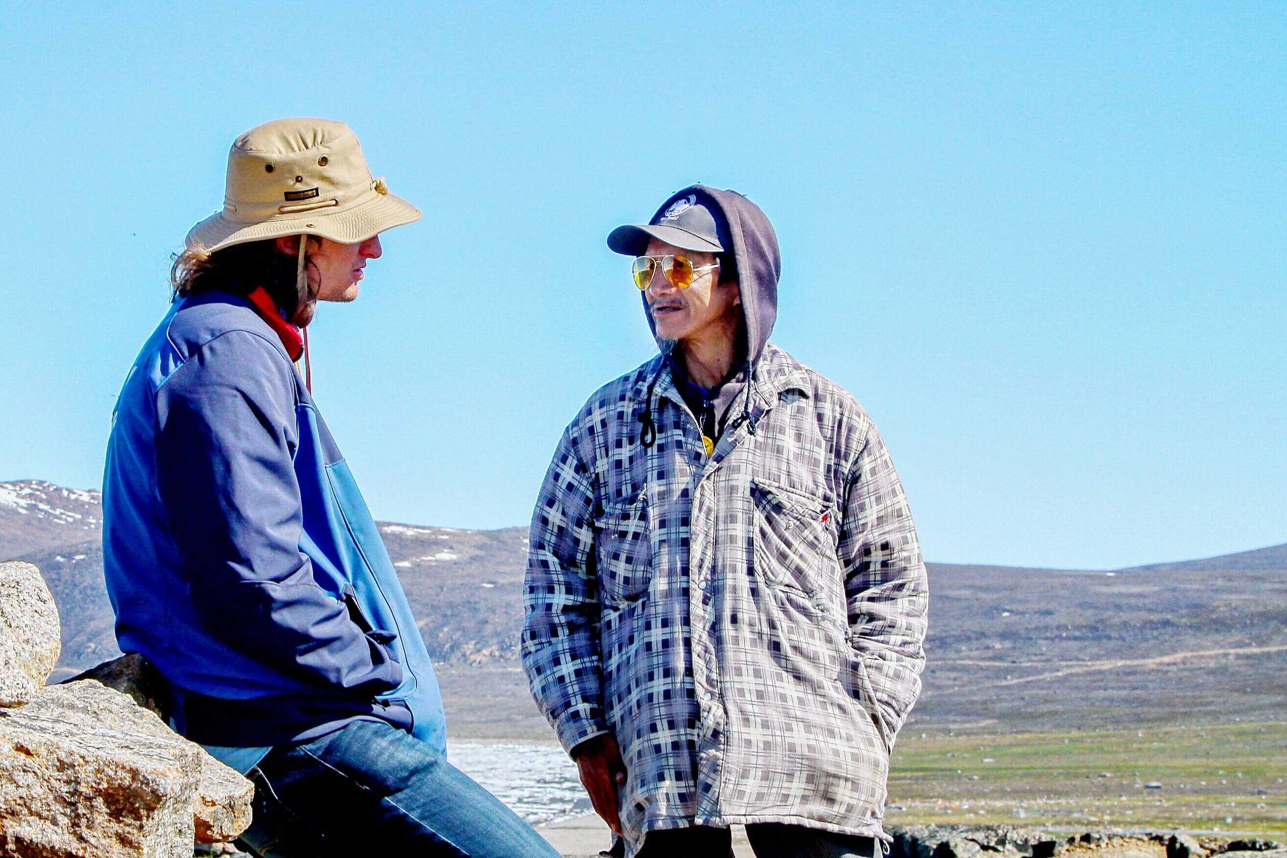 Two men talking to each other against a hilly background and blue sky