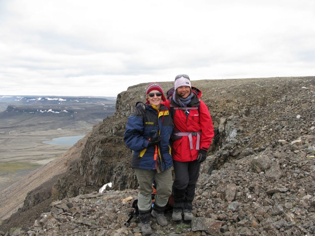 Two women in hiking gear in rocky, hilly landscape against a cloudy sky