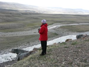 Person with red jacket and white hat standing in a barren landscape with river