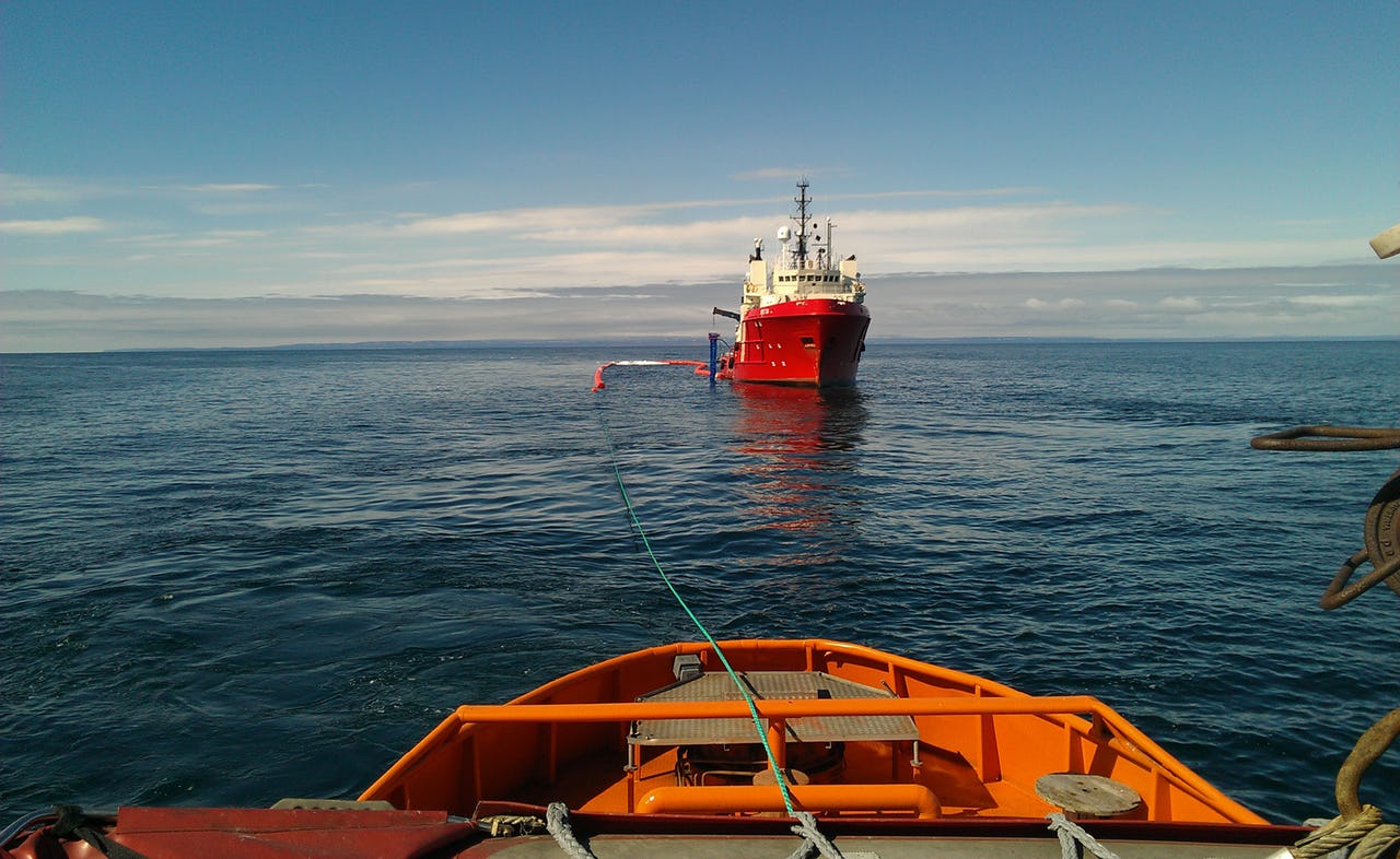 Two boats setting out a skimmer during an oil spills' response exercise in Kirkenes, Norway, against a blue sky and calm sea