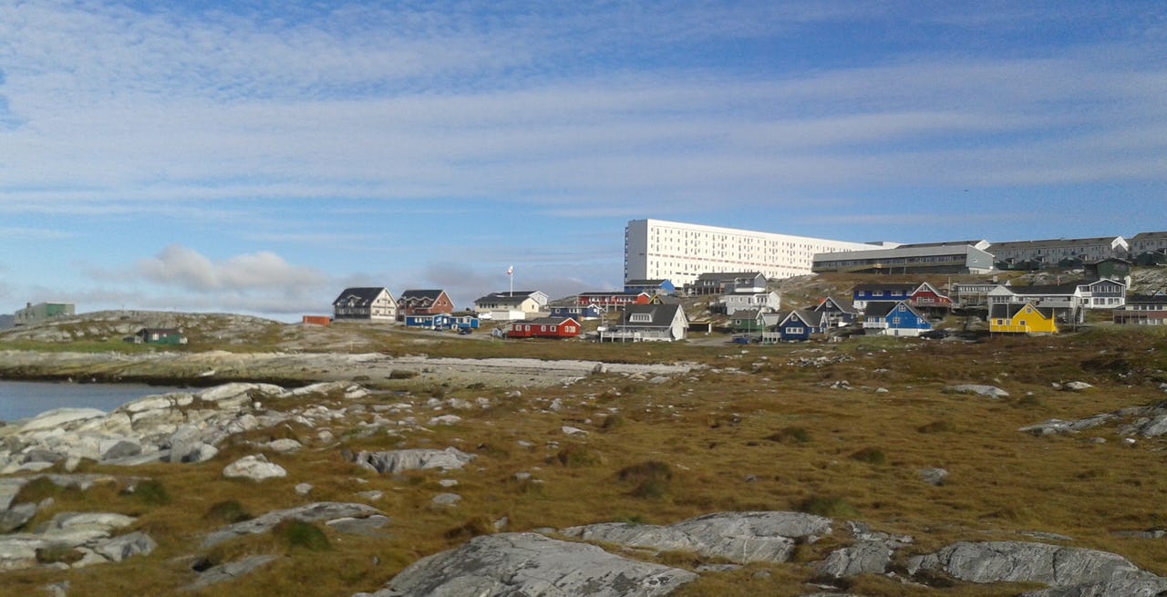 Colorful houses and buildings in Nuuk, Greenland on flat rocky terrain with the sea on the left hand side