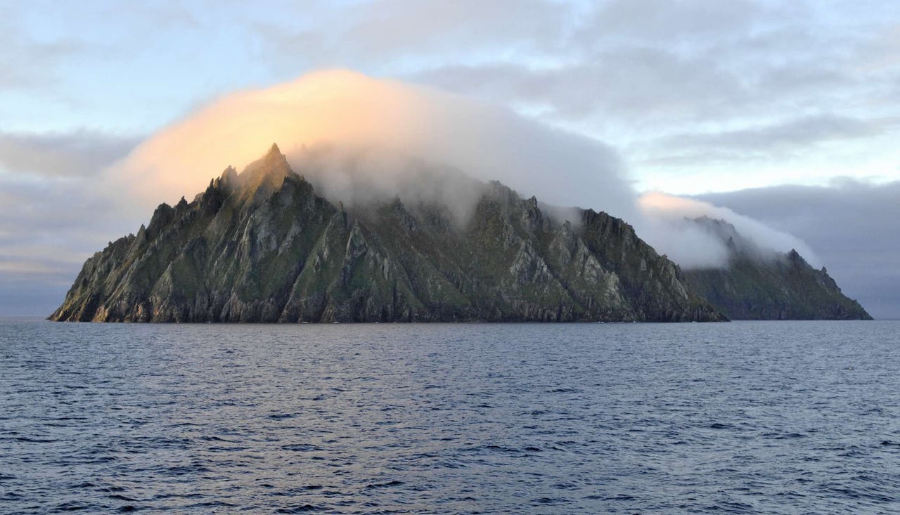 Island of rock with water around and fog in front of island