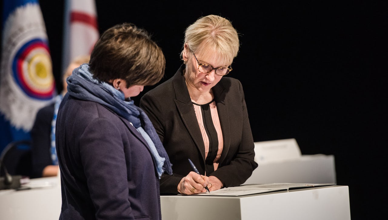 A woman signing a statement watched by another woman
