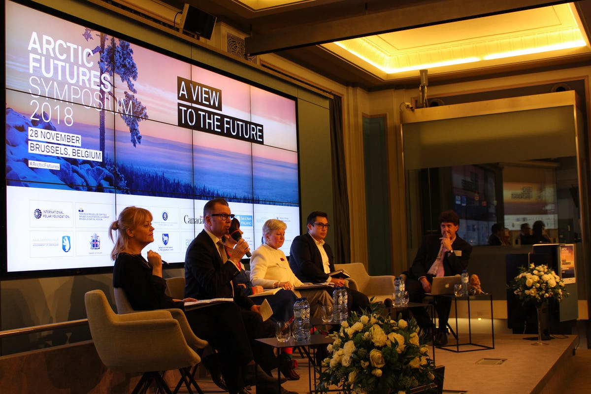 Women and men sitting in chairs on a panel with screen in the background