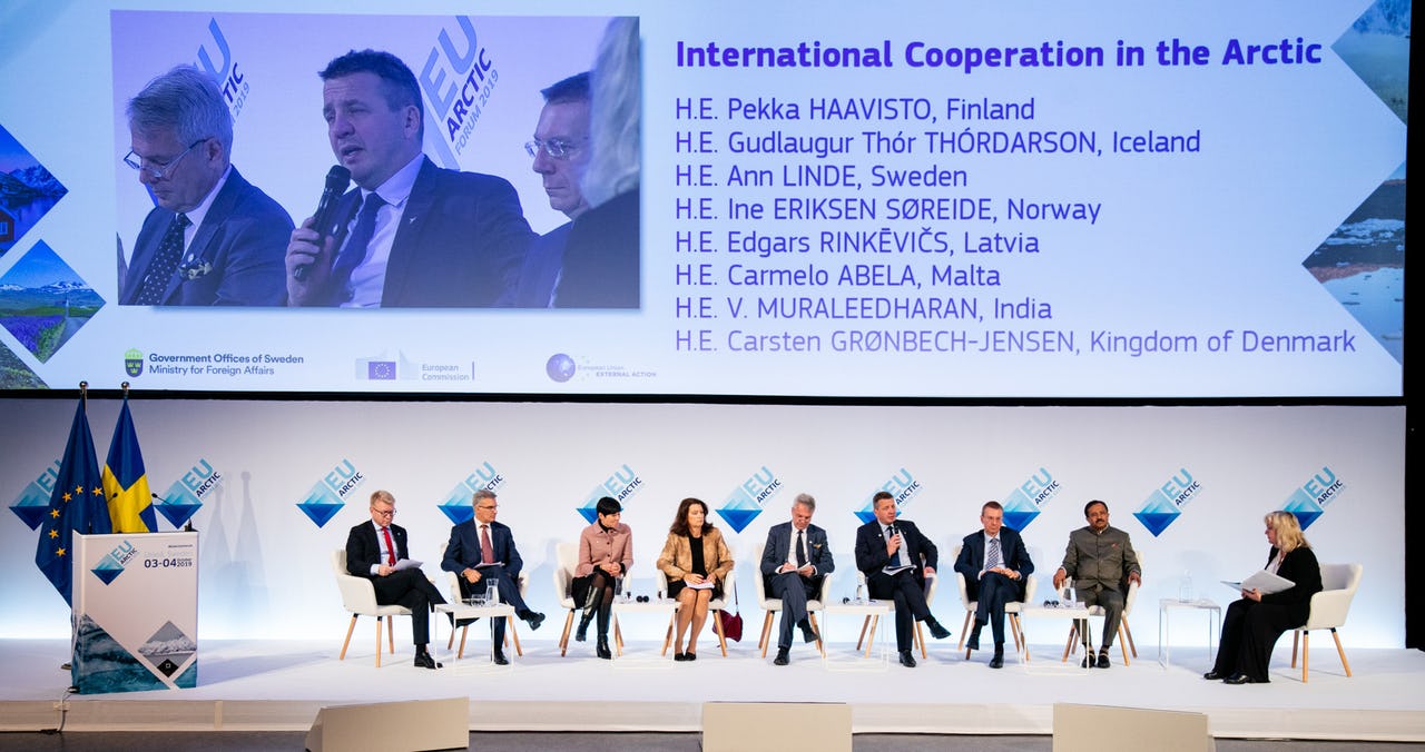 6 men and 3 women sitting on a stage with a huge screen behind them