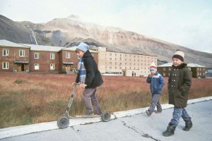 Three small boys walking in front of a mountain and some houses