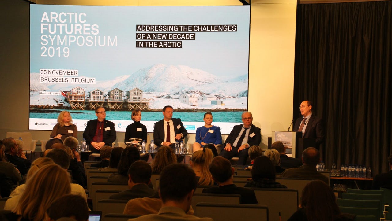 Man presenting at conference with other panellists sitting on chairs next to him