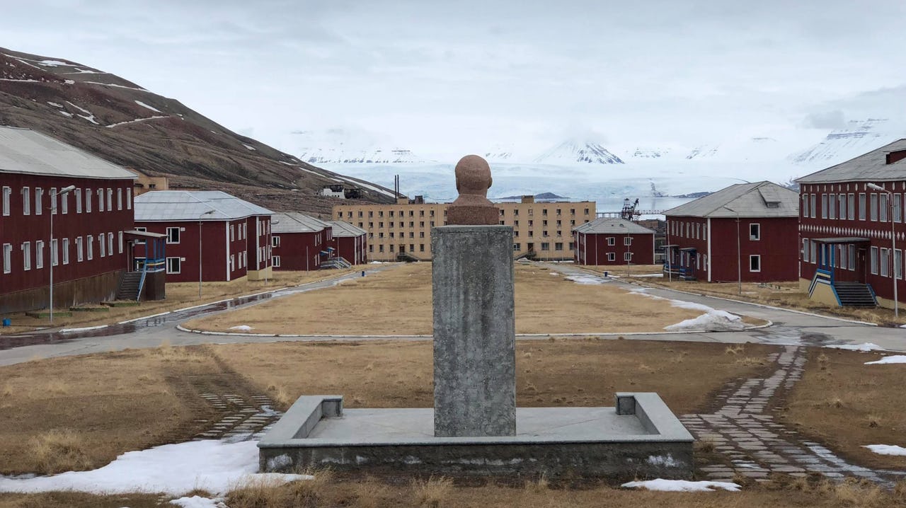 A statue faces some buildings in front of a glacier