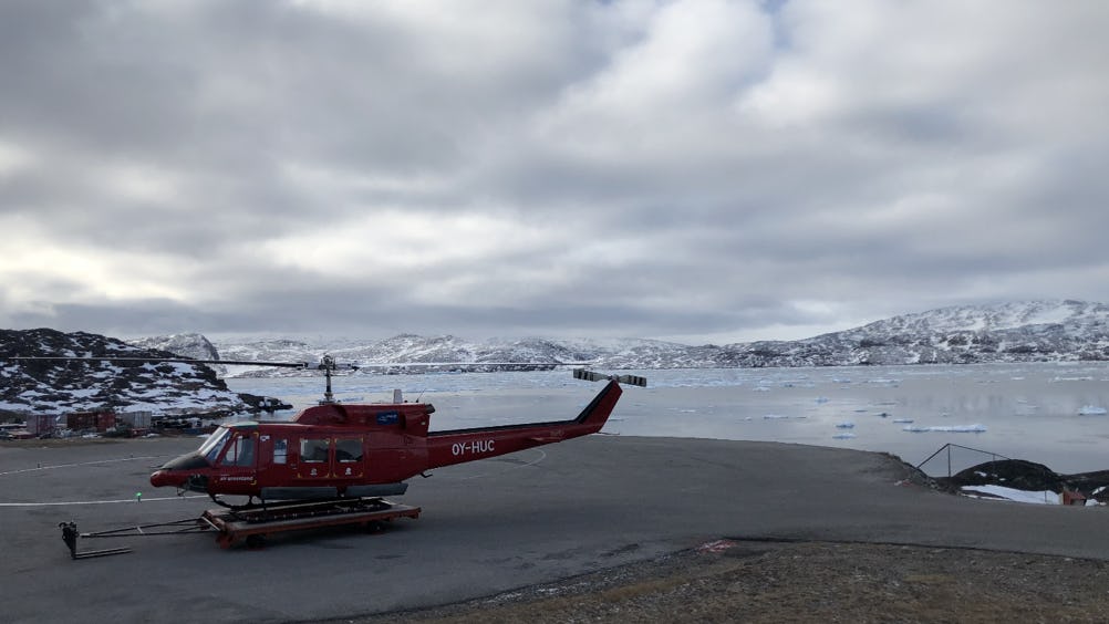 A helicopter ready to leave from Qaqortoq heliport which overlooks ice-infested waters and rolling snowy hills on an overcast day
