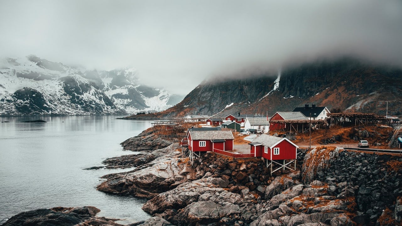 Small cabins in red and white at the seaside with snowy mountains in the back