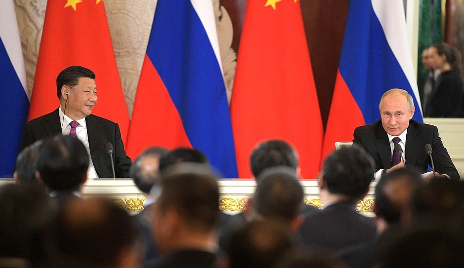 Two men in suits talking to press in front of some Russian and Chinese flags