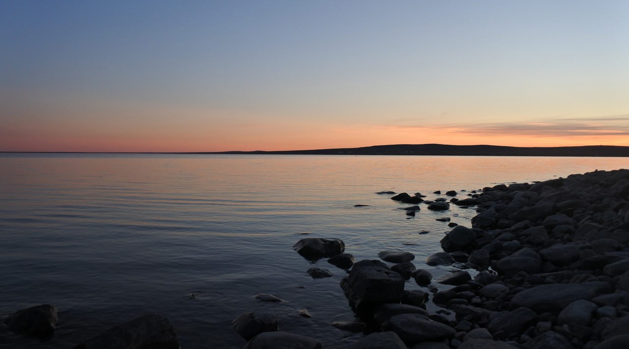 Sunset on water with rocks and mountain