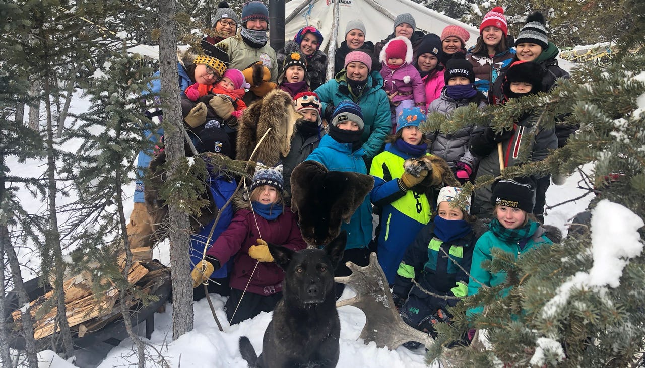 Group of people and dog in front of a tent in a forest during winter