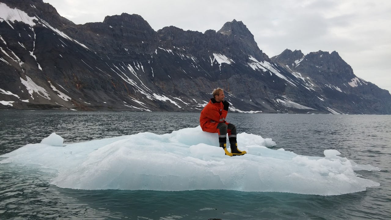 Andreas Østhagen sitting on an iceberg with mountains in the background wearing red winter gear