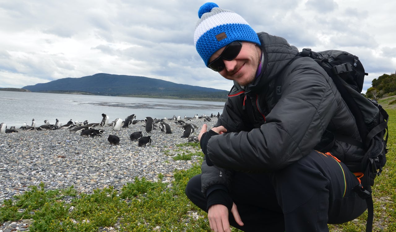 Man wearing a pair of dark sunglasses and a blue beanie with penguins and mountains in the background