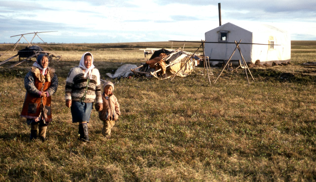 Two Arctic Indigenous reindeer herding women and a child of the Dolgan tribe stand in front of their field nomad camp in Northern Krasnoyarsk Krai, Russia