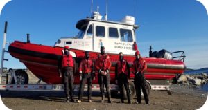 5 men wearing face maskes standing in front of a boat in red and white onshore
