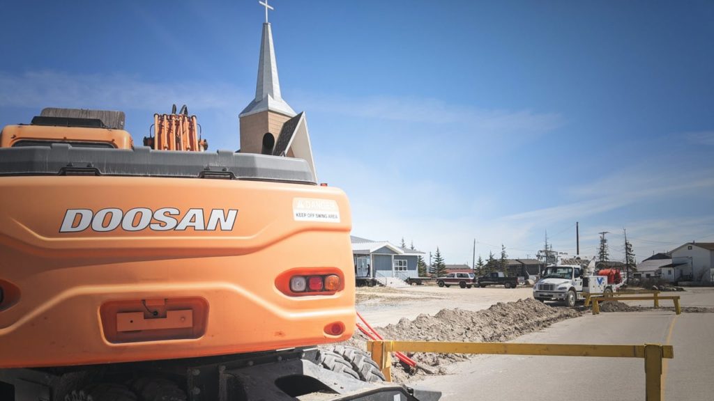 An orange vehicle with a church and a construction site behind it