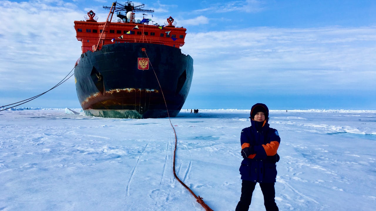 Woman in polar clothing standing on Arctic ice with Russian icebreaker in the background