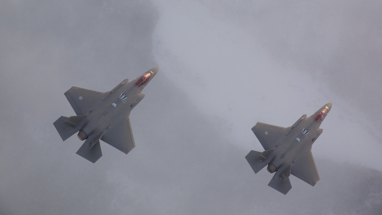 Two grey fighter jets flying upwards next to each other