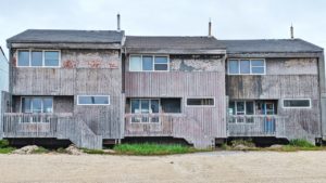 Three dilapidated houses painted grey on a gravel road