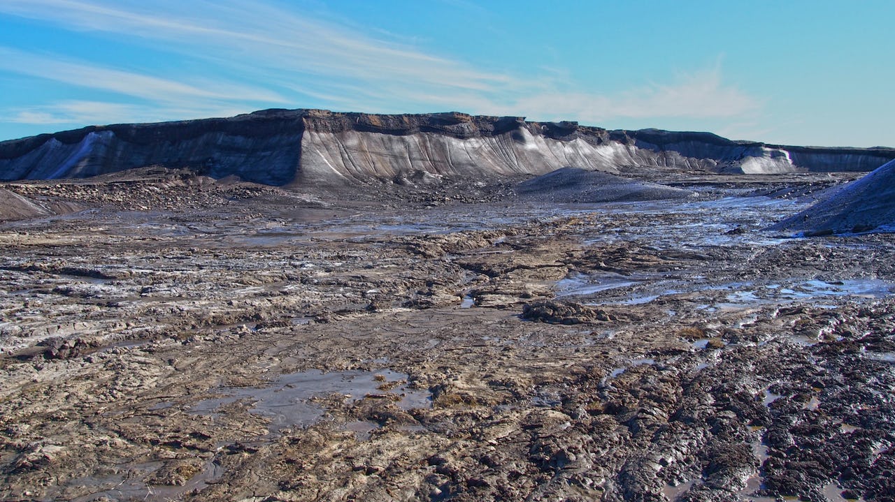 A wall of permafrost against a blue sky with mud in the foreground