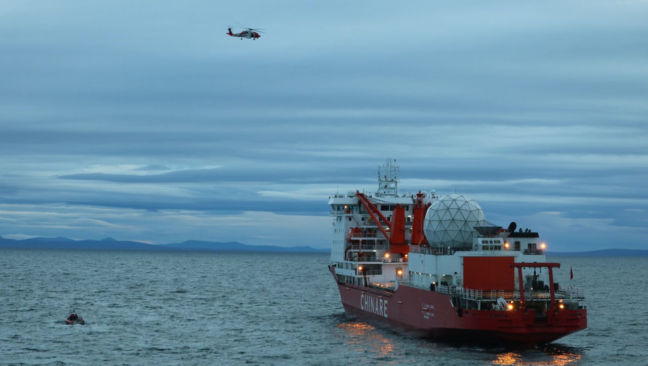 United States Coast Guard helicopter and small boat crew over Chinese Arctic and Antarctic research vessel Xue Long in the ocean off the coast of Nome Alaska