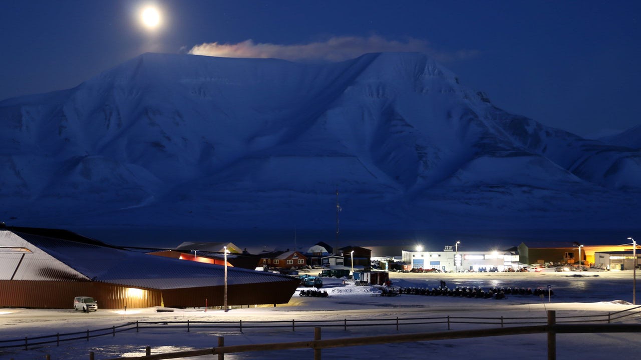 A moonlit view over Longyearbyen, Svalbard with buildings in the foreground and snowy mountains in the background