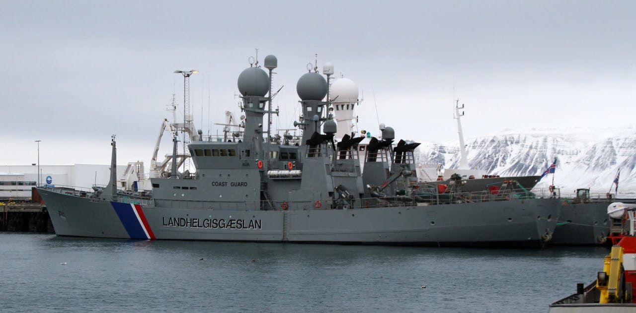 Grey coast guard vessels with Icelandic blue white and red diagonal stripes on the hull with seafront and snowy mountain background