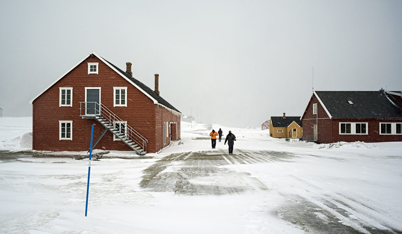 People walking through the snow between red buildings against a grey sky