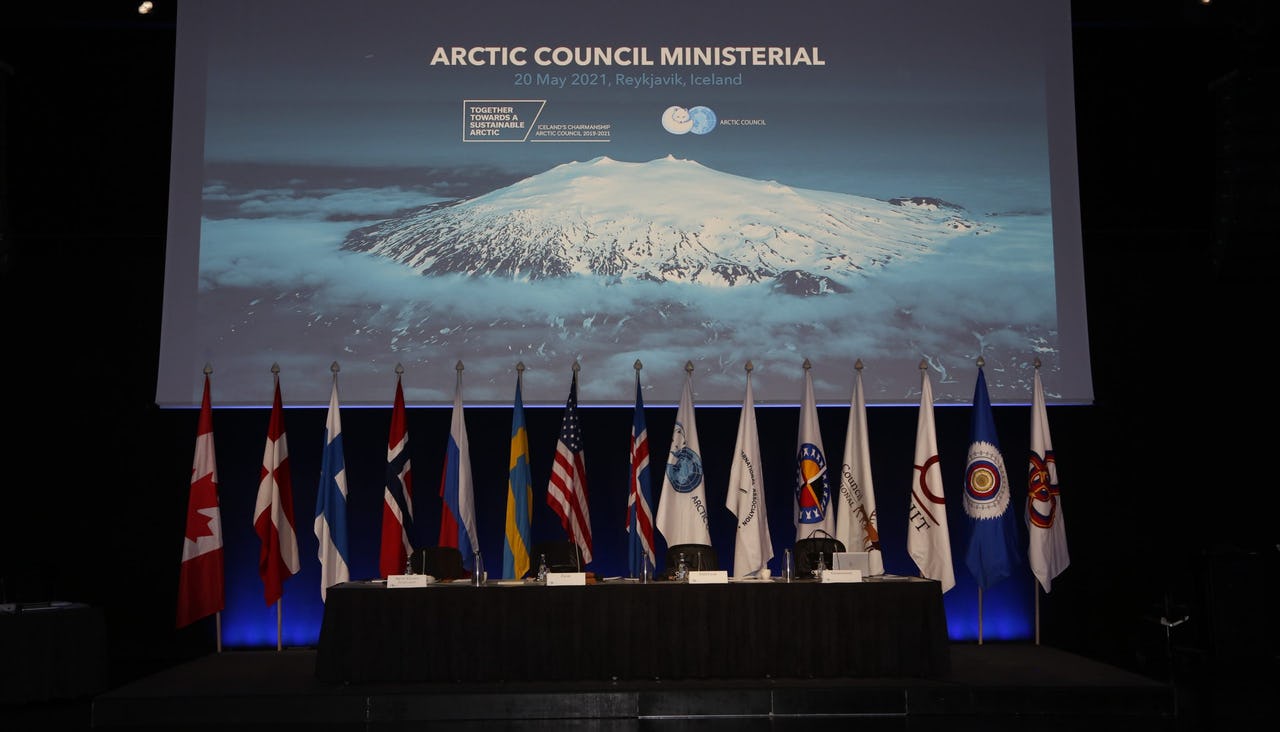 Flags of all permanent Arctic Council members in one frame and in front of an image of an snow-covered mountain