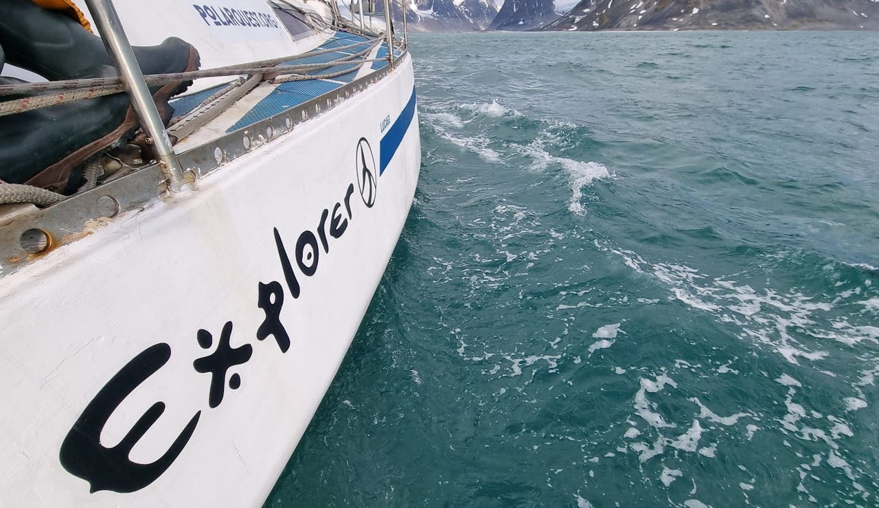 Zoomed in picture of a white skipper boat with blue waves and snowy mountains in the background