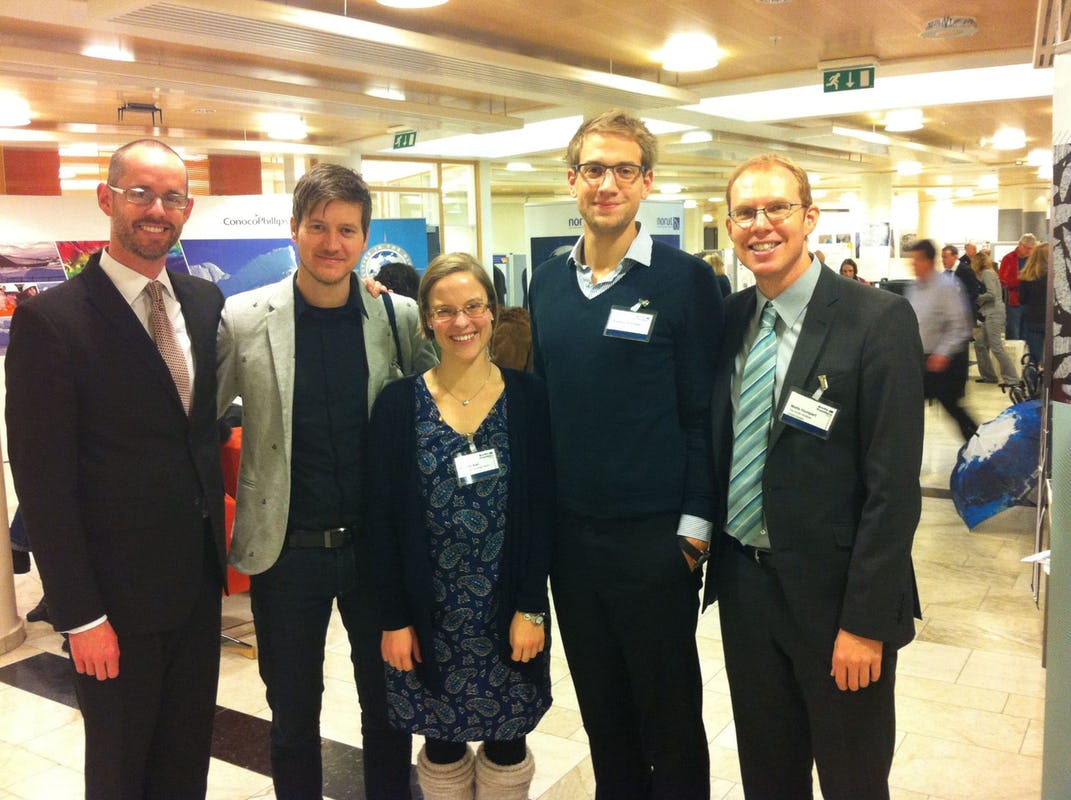 1 woman and 4 men posing for a group picture in a venue hall