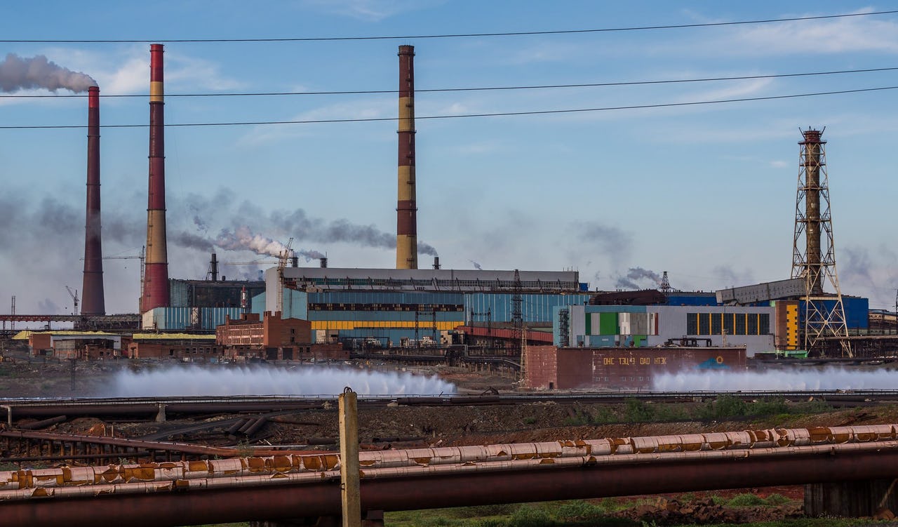 Rust-colored factory with smoking pipes against a blue sky