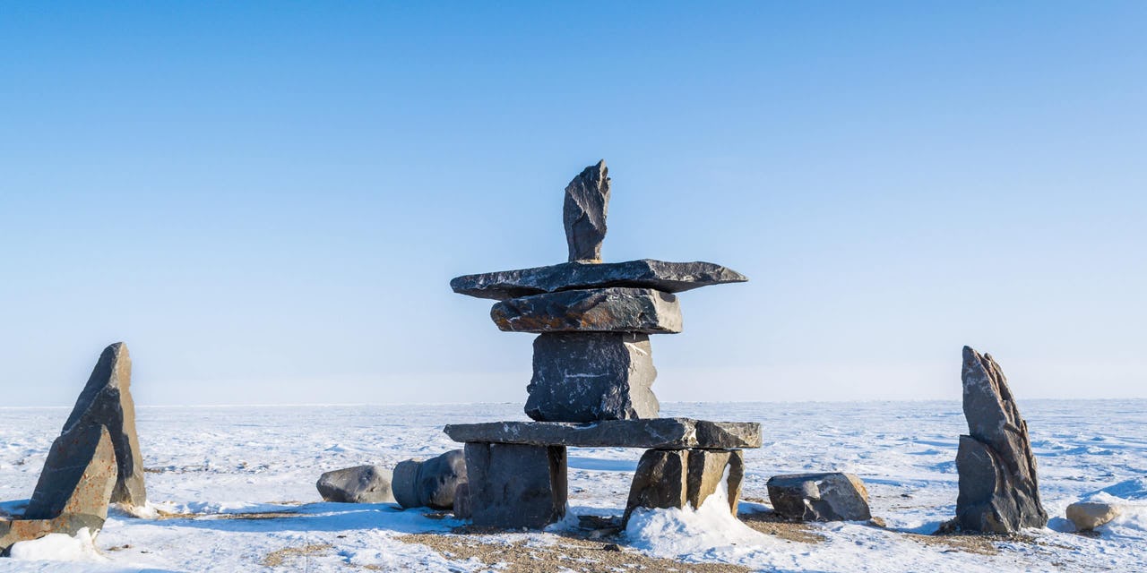 A grey stone Inukshuk against a blue and white icy background