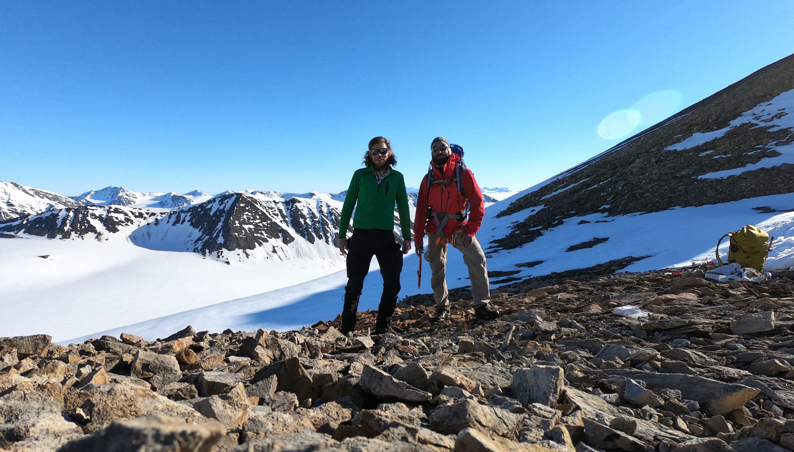 Two mountaineers - Max Kortmann and Sebastian Pohl - in colorful winter gear with snowy mountains in the back