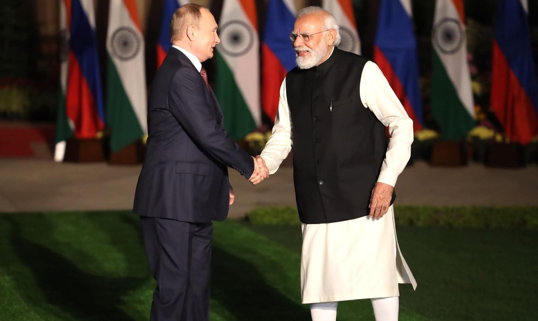 Vladimir Putin greeting Narendra Modi by handshake with Russian and Indian flags in the background