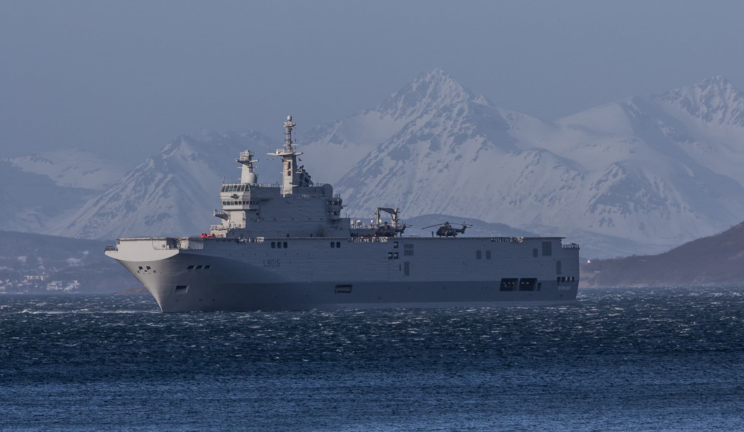 French amphibious assault ship Dixmude sailing through Arctic waters with snowy mountains in the back